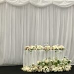 The starlight backdrop is part of this wedding staging is created by Fabulous Functions UK and included a sweetheart table decorated with an abundance of flowers. There were flowers on the table, flowers surrounding the table and two floral arrangements on pedestals either side if the sweetheart table