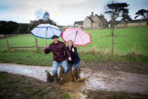 Couple under umbrellas splashing in mud